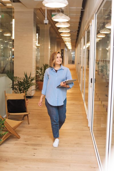 woman holding tablet walking in hallway of office building
