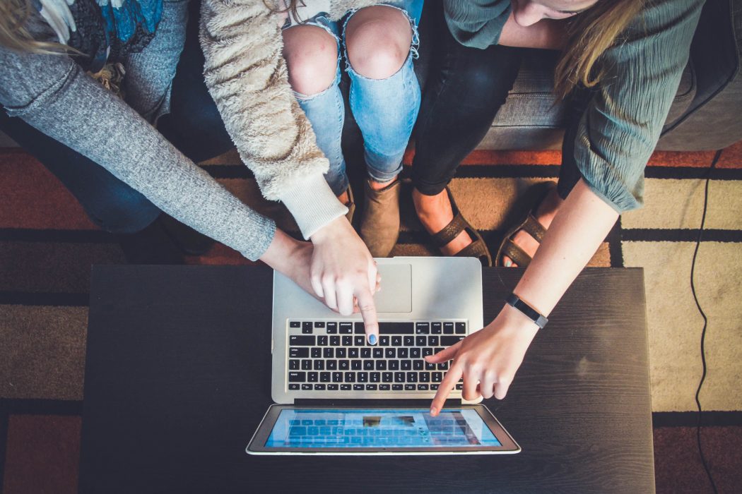 Three people sitting on a couch pointing at laptop screen aerial view