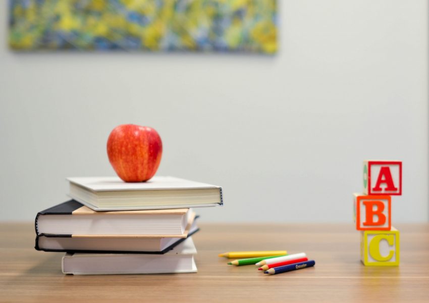 stack of three books on a desk with a red apple on top and a, b, c block cubes to the side