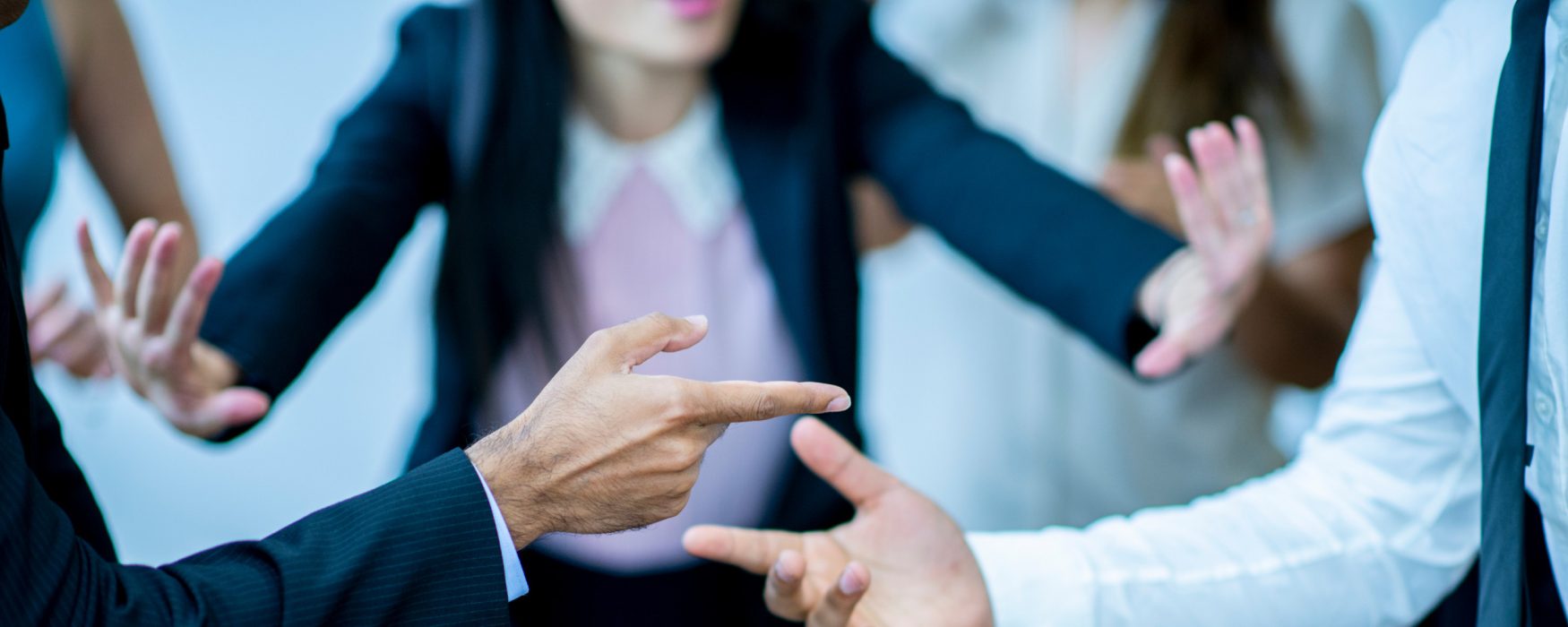 Two mean pointing fingers at one another while a woman puts her hands up in an attempt to stop the argument.