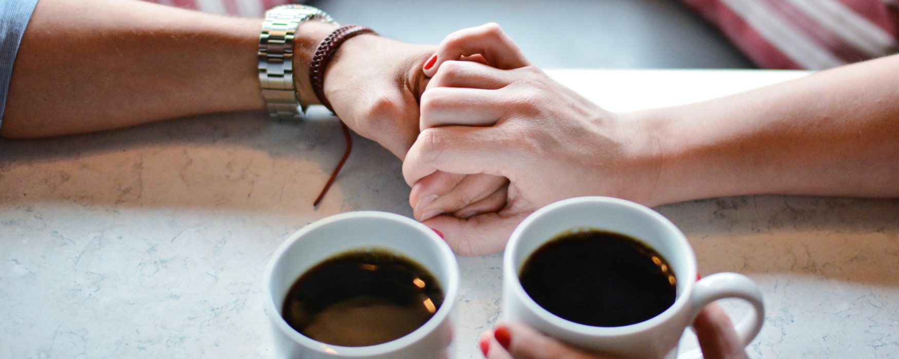 Two people holding hands over a cup of coffee
