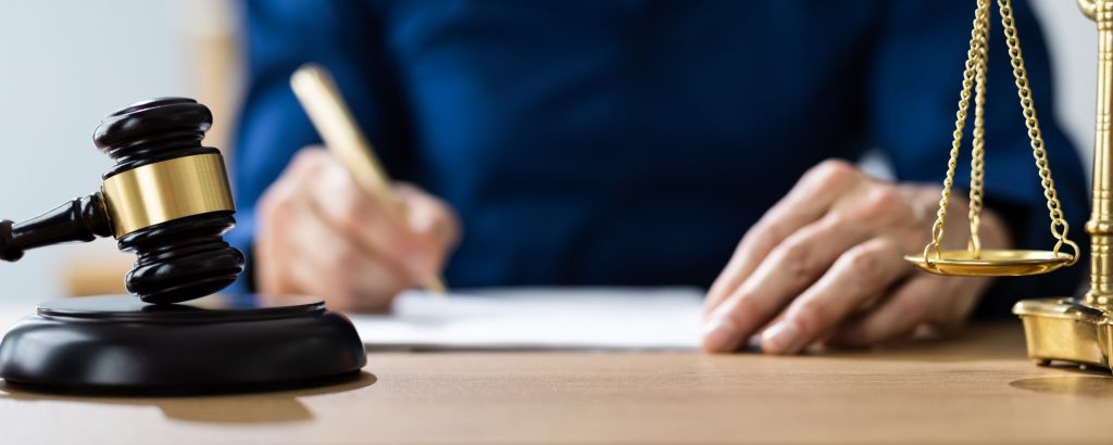 A woman's hand are pictured holding a pen over a piece of paper that is placed on a desk.