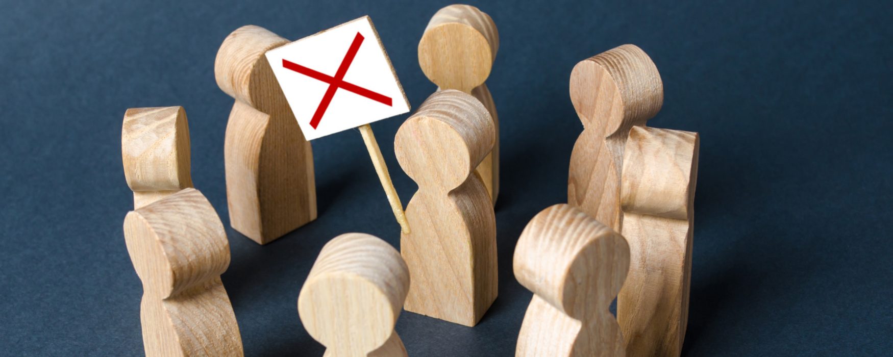 Image of a grouping of wooden blocks shaped like people, one holding a sign with a red X on it