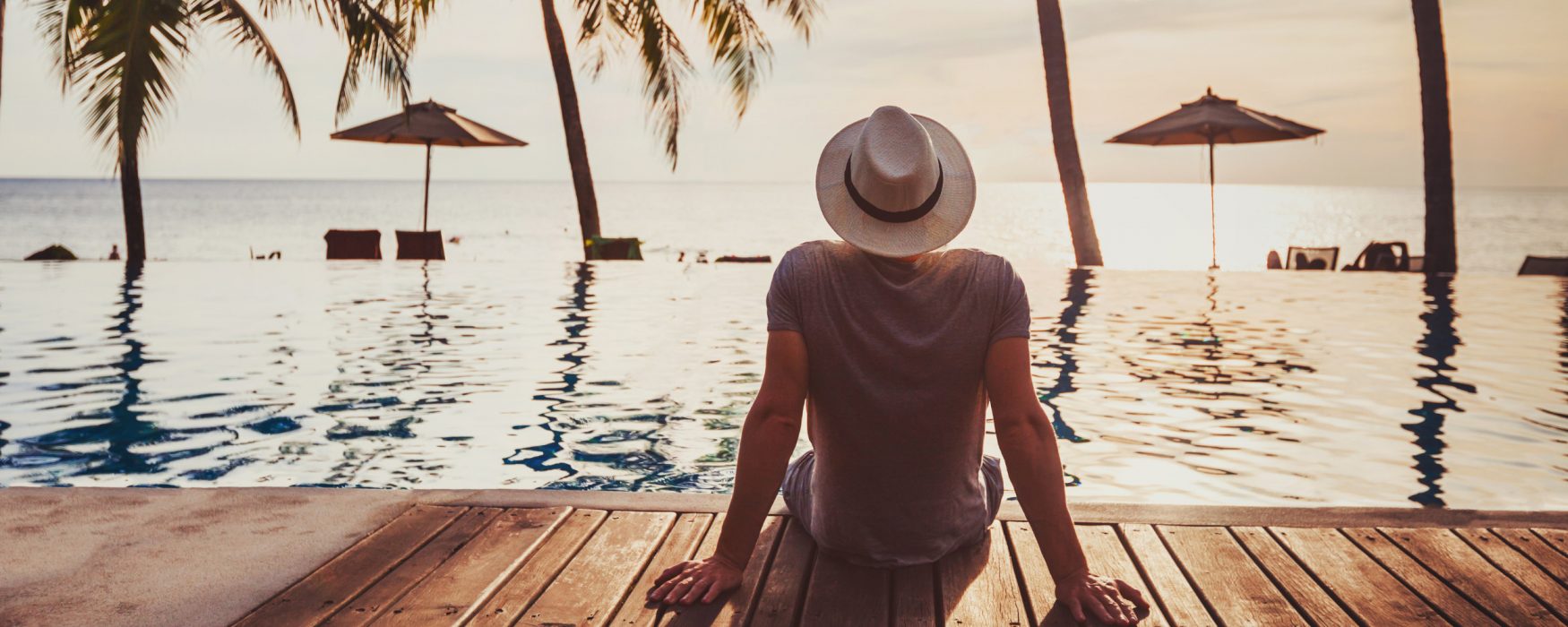 Image of a person sitting near the water under palm trees while on vacation