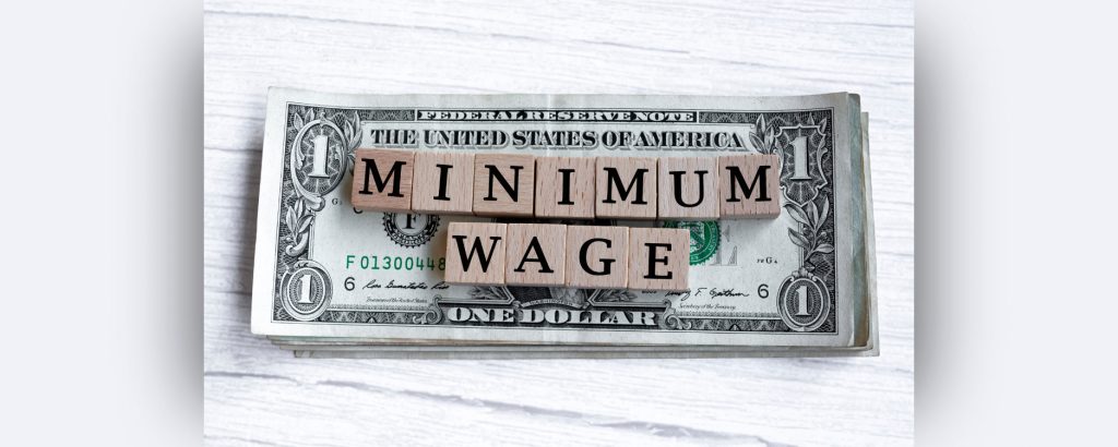 One dollar bills on a table with blocks on them spelling minimum wage