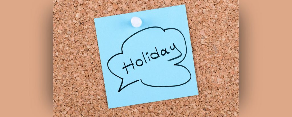 Note with the word holiday on it pinned to a bulletin board