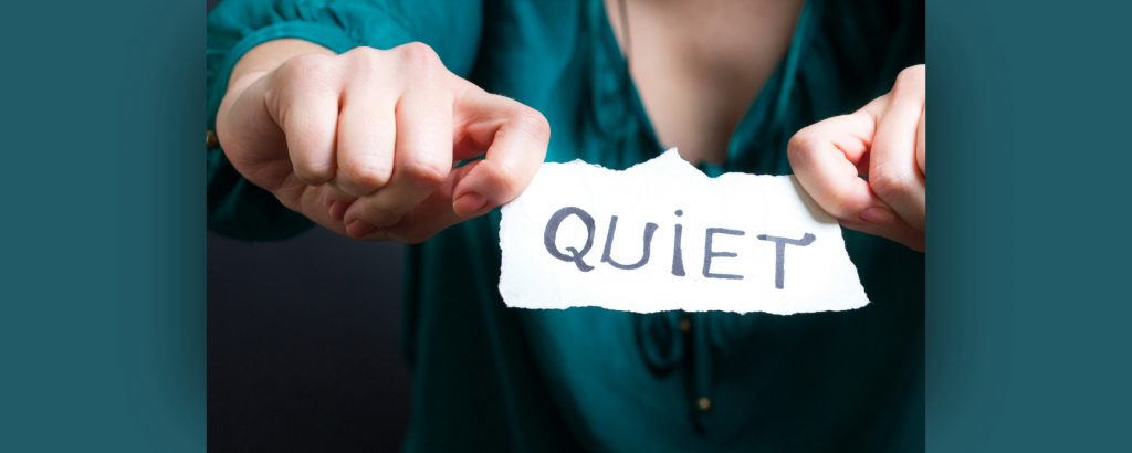 Person holding a piece of paper with the word quiet written on it