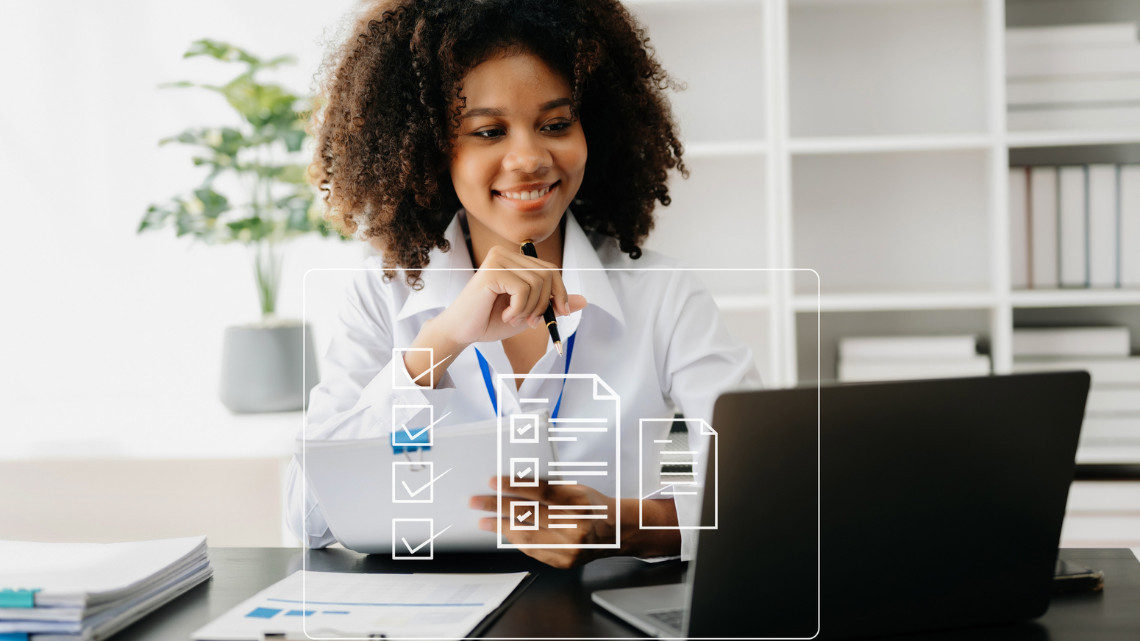 An African American woman sits at a desk with an open laptop in front of her.