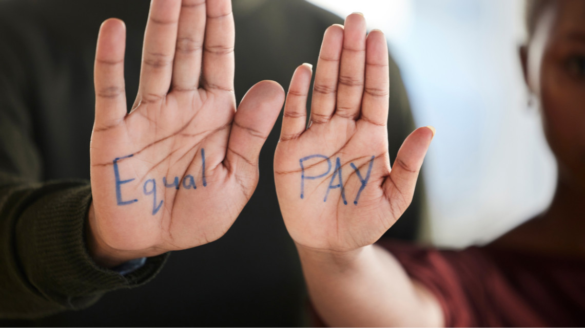 A man and a woman each holding up one hand with equal pay written on them to illustrate discrimination and steering