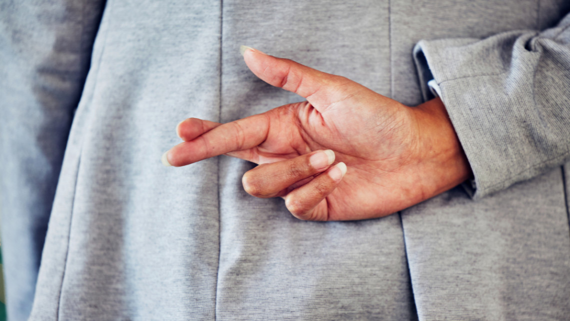 A person crosses their fingers behind their back, representing a lying in an interview