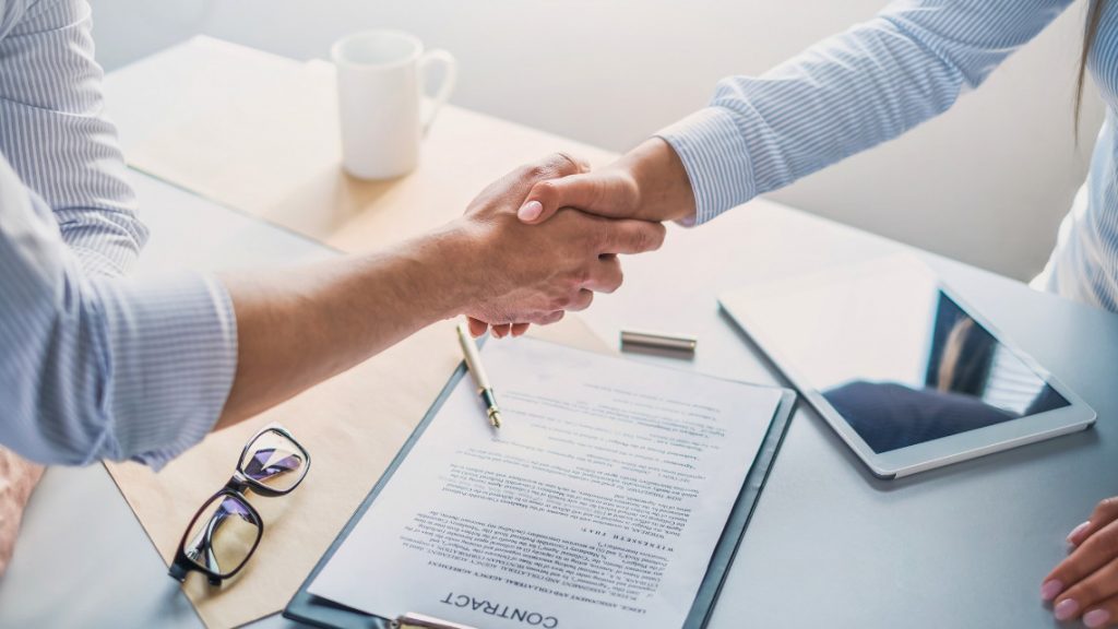 Two people shaking hands over an employment contract